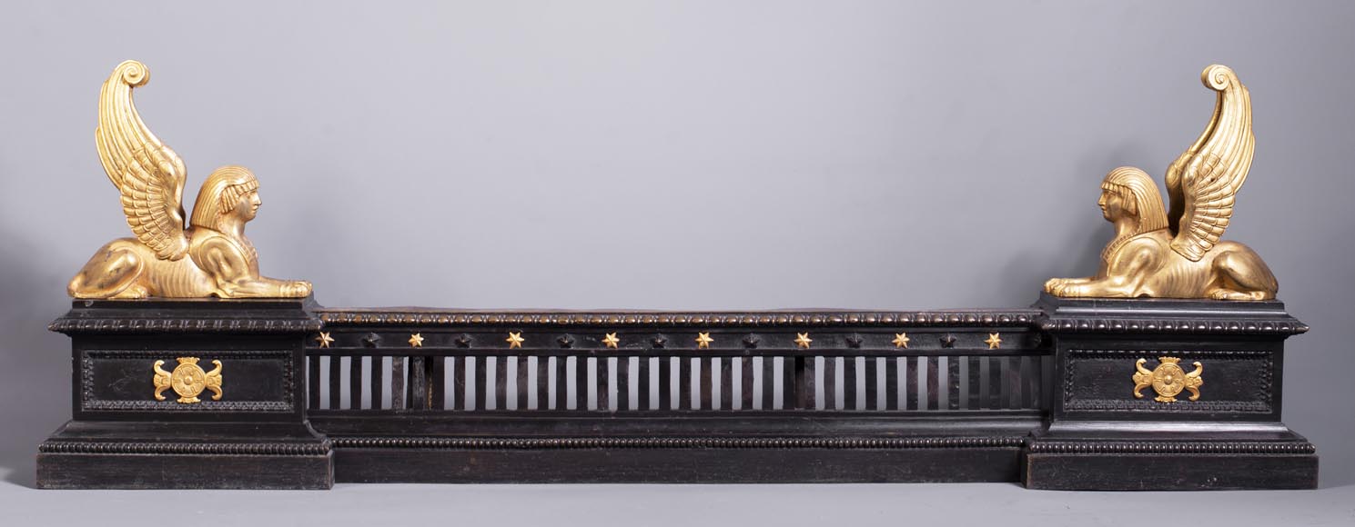 Barre de chenets aux sphinx ailés en bronze à deux patines Barre de chenets aux sphinx ailés en bronze à deux patines-0